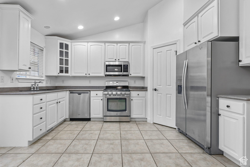 Kitchen featuring light tile patterned floors, stainless steel appliances, lofted ceiling, dark countertops, and a sink