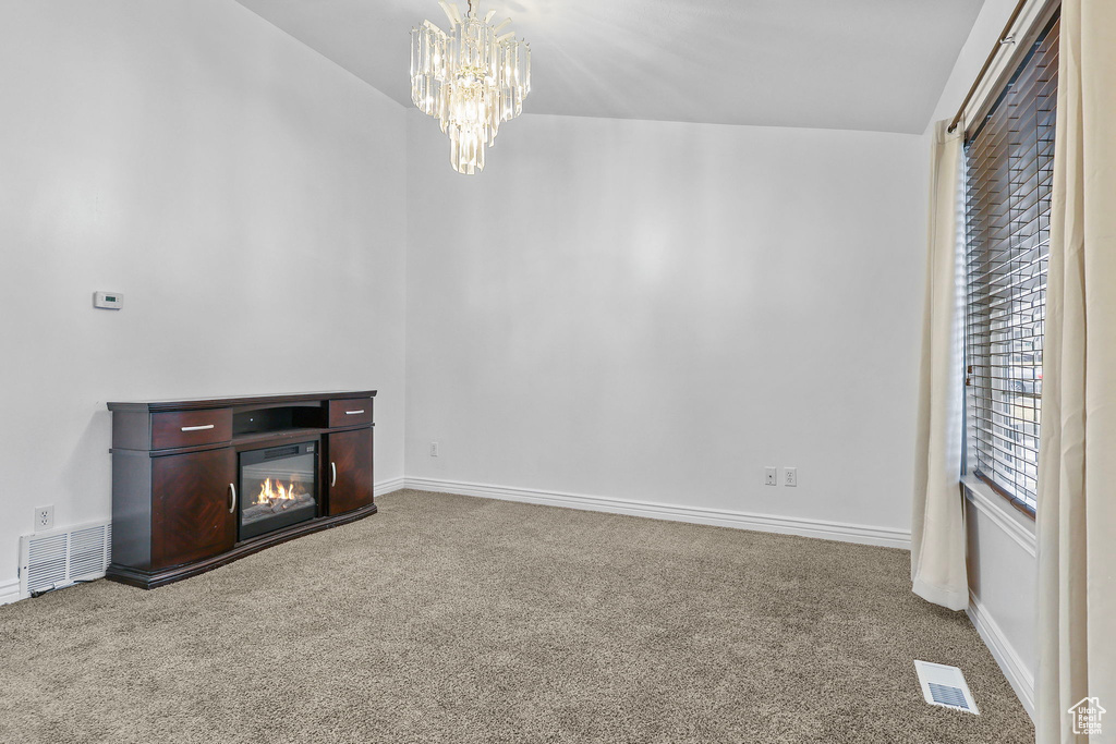 Unfurnished living room featuring carpet floors, visible vents, and a notable chandelier