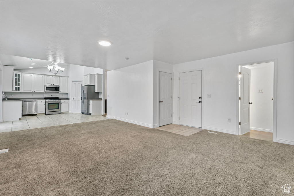 Unfurnished living room featuring light carpet, a sink, a notable chandelier, and light tile patterned floors