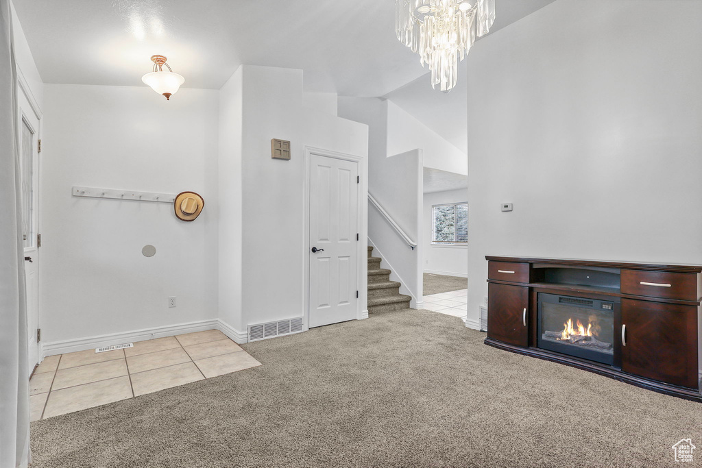 Unfurnished living room with carpet floors, tile patterned flooring, visible vents, and stairs