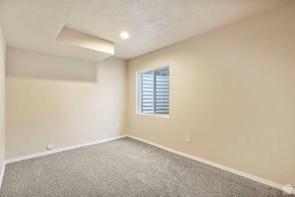 Carpeted empty room featuring a textured ceiling and baseboards