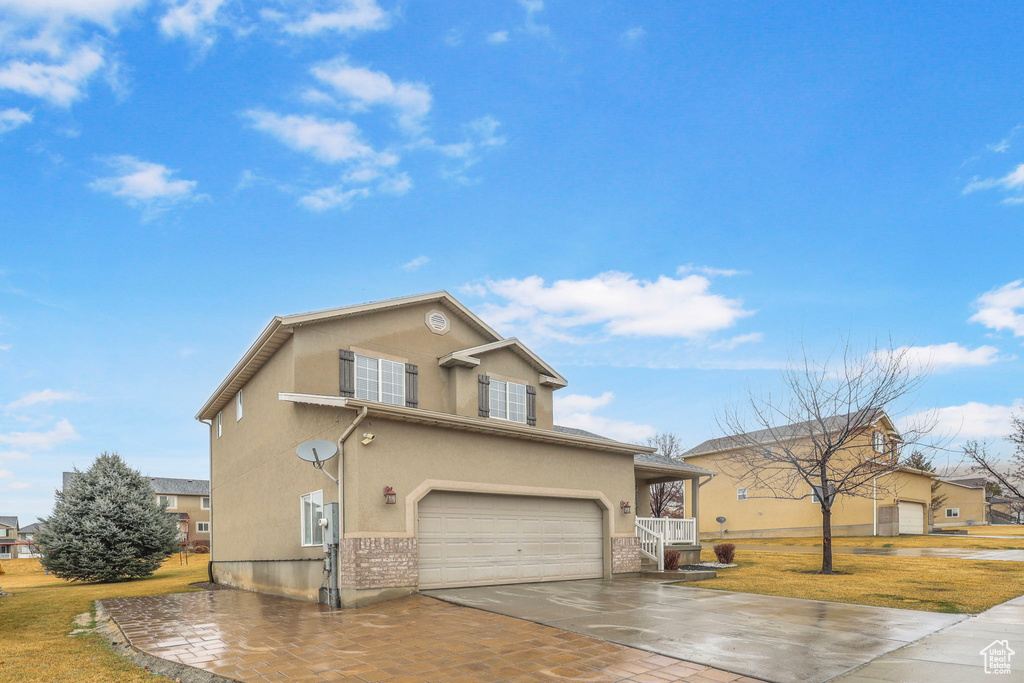 Traditional home featuring an attached garage, a front lawn, decorative driveway, and stucco siding