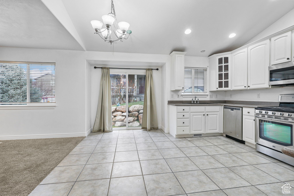 Kitchen featuring stainless steel appliances, dark countertops, light colored carpet, white cabinetry, and a sink