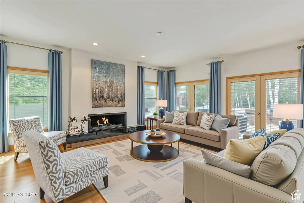 Living room with wood finished floors, a warm lit fireplace, recessed lighting, and french doors
