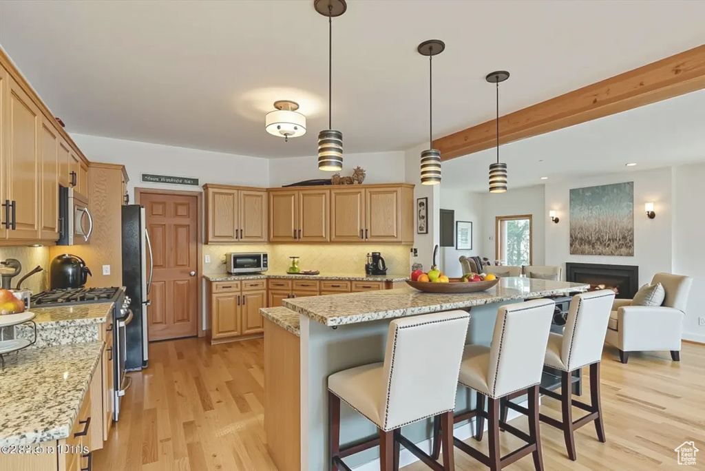 Kitchen with stainless steel appliances, a kitchen breakfast bar, light wood-type flooring, open floor plan, and decorative backsplash