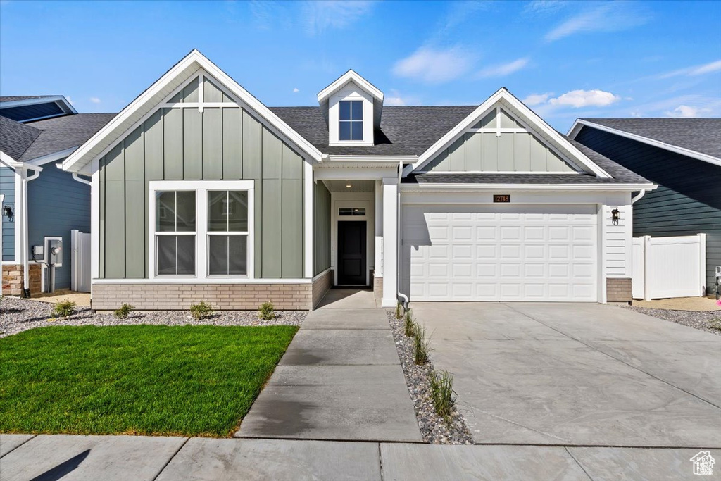 View of front of home featuring driveway, fence, brick siding, board and batten siding, and a garage