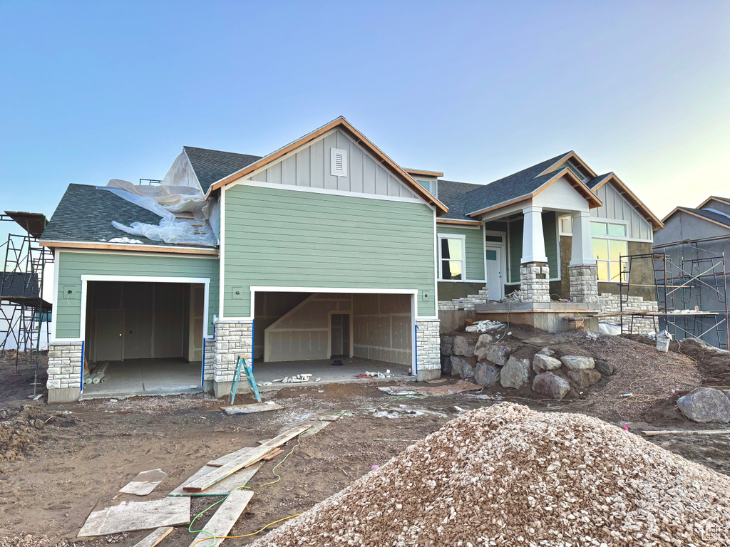 Craftsman-style house featuring an attached garage, stone siding, a shingled roof, and board and batten siding