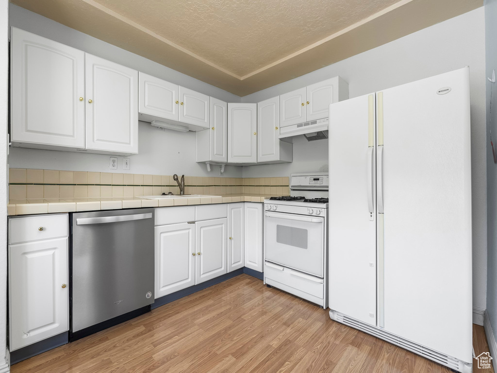 Kitchen featuring white appliances, a sink, white cabinets, under cabinet range hood, and light wood-style flooring