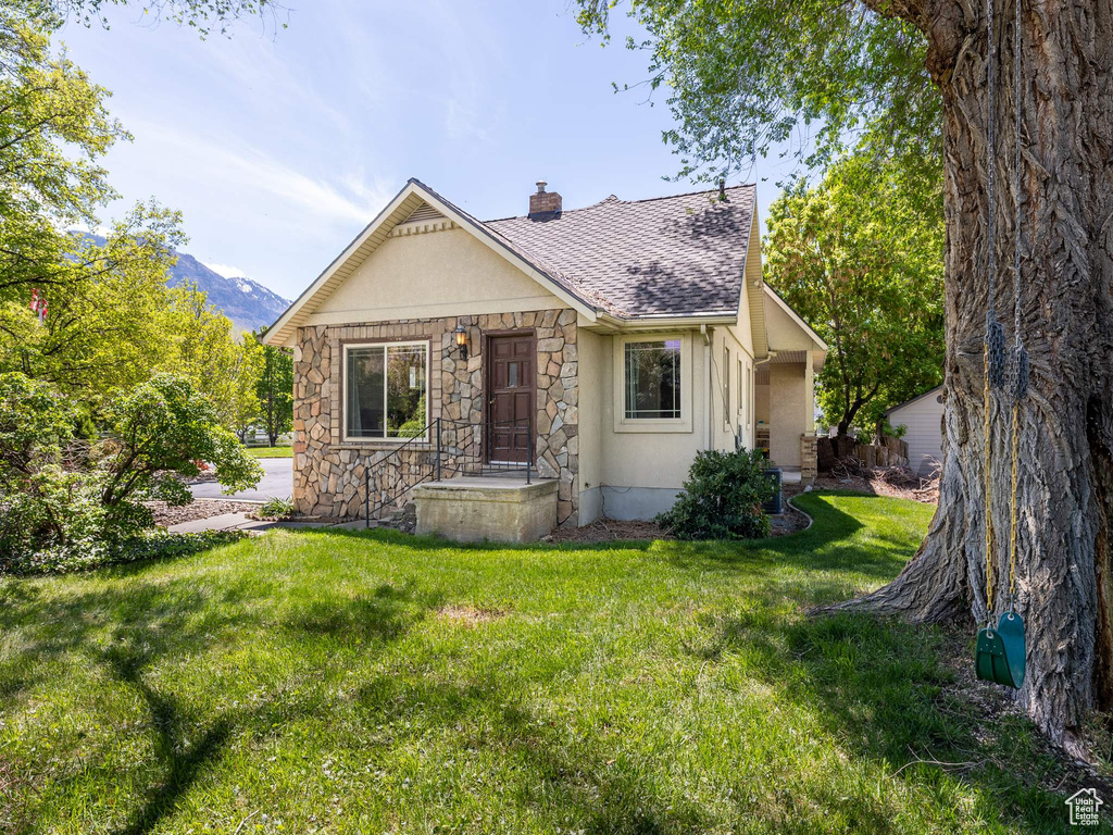 English style home with a chimney, a front yard, stone siding, roof with shingles, and stucco siding