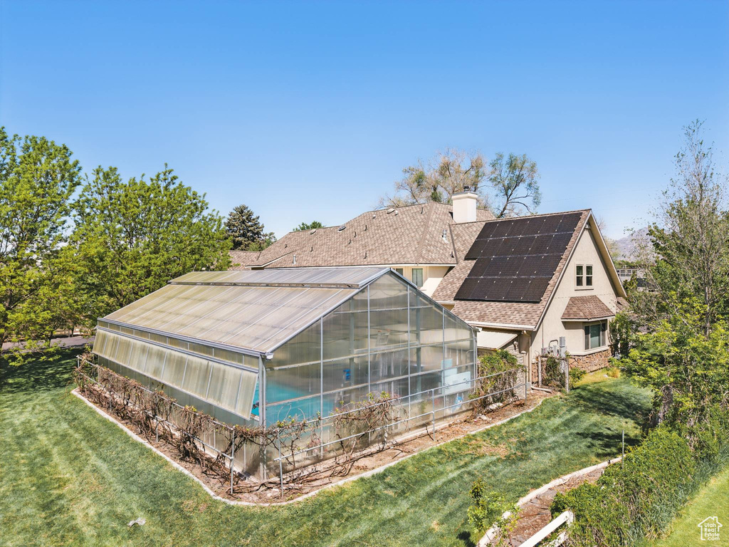 Rear view of house with a greenhouse, a chimney, roof mounted solar panels, an outdoor structure, and a yard