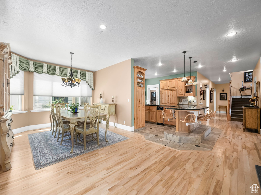 Dining room featuring baseboards, light wood-style floors, a chandelier, a textured ceiling, and stairs