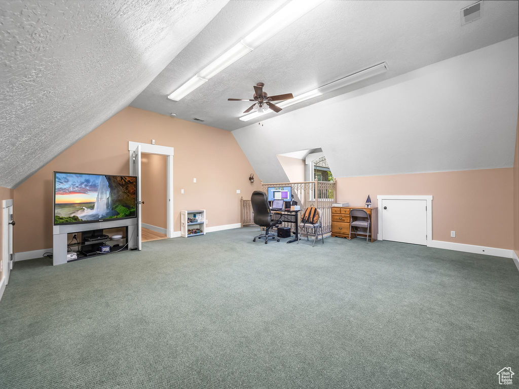 Carpeted home office featuring vaulted ceiling, a ceiling fan, a textured ceiling, and baseboards