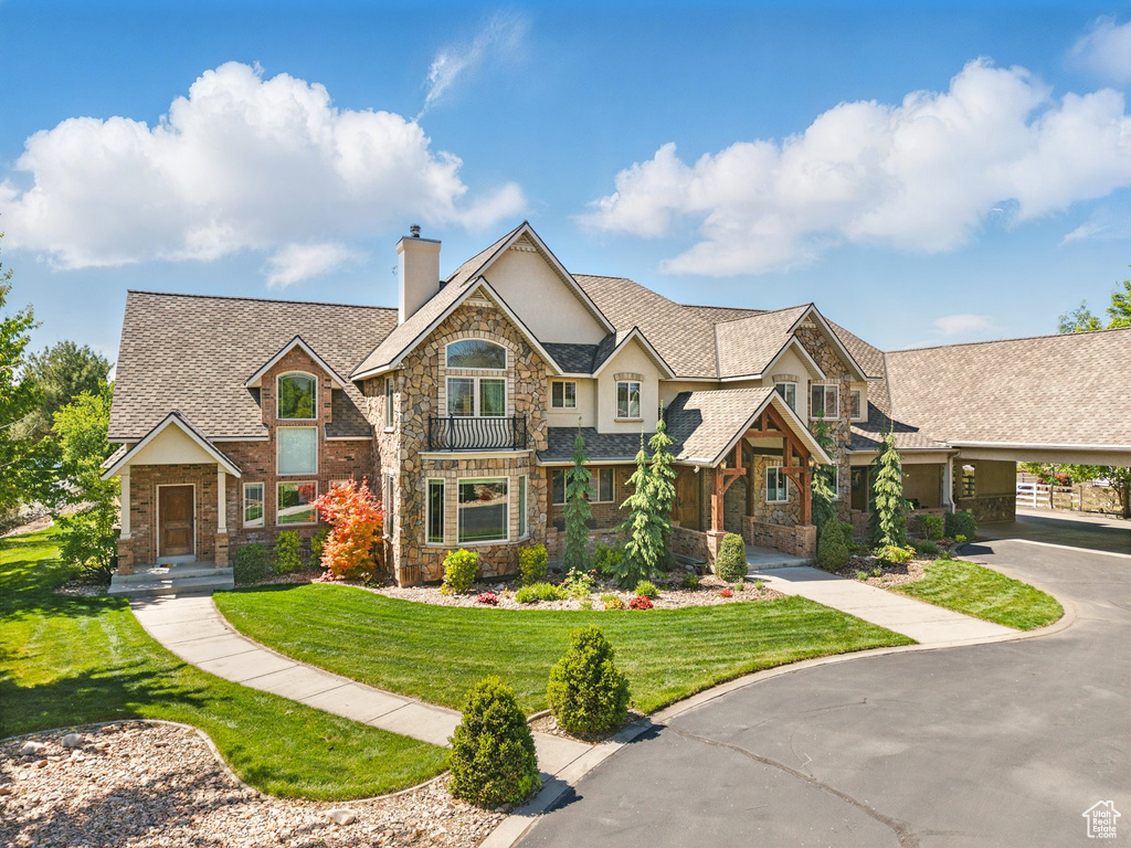 View of front facade featuring stone siding, a chimney, stucco siding, a front lawn, and driveway