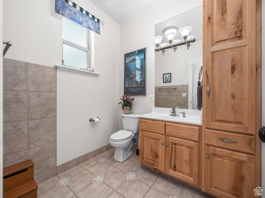 Bathroom featuring toilet, tile patterned flooring, vanity, tile walls, and baseboards