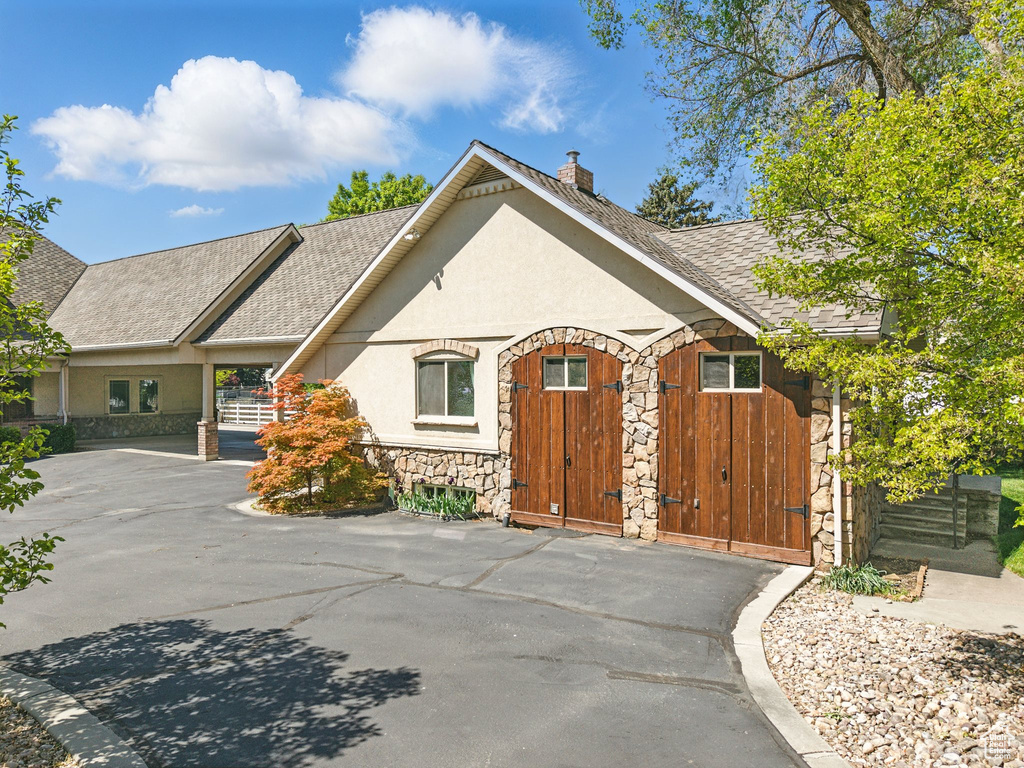 View of front of property featuring stone siding, stucco siding, a chimney, and roof with shingles