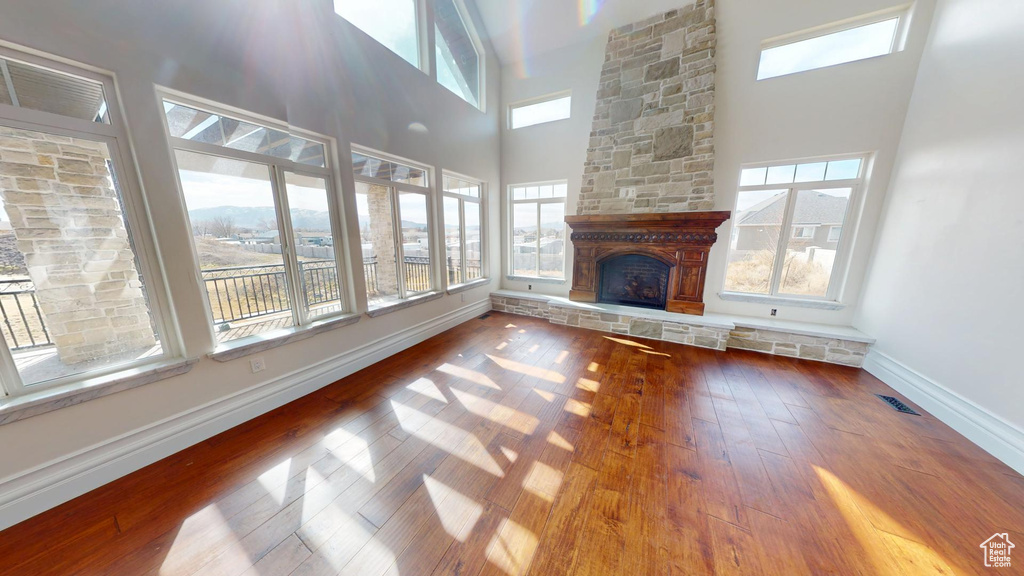Unfurnished living room featuring visible vents, a stone fireplace, baseboards, and hardwood / wood-style flooring