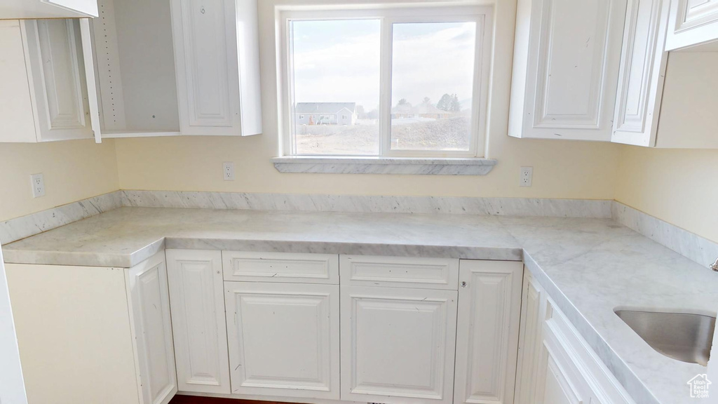 Kitchen featuring light stone counters, white cabinets, and a sink