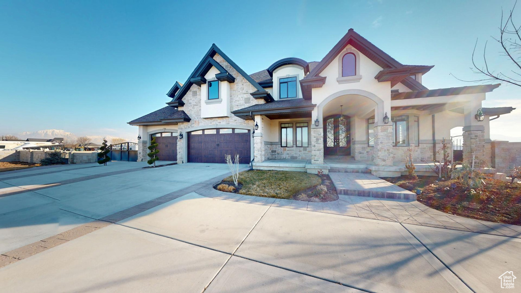 View of front of house featuring a garage, stone siding, french doors, driveway, and stucco siding