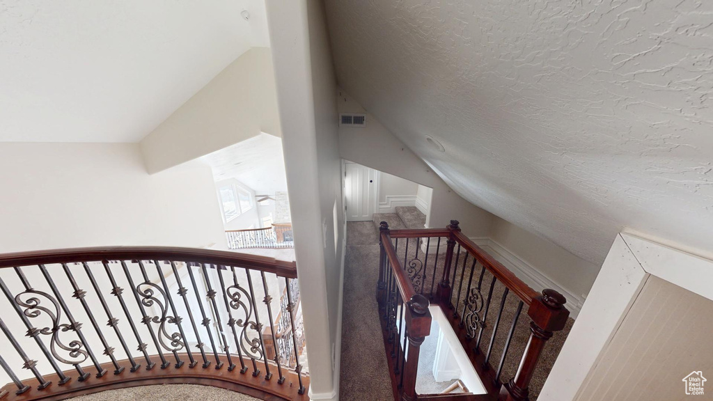 Stairway featuring visible vents, vaulted ceiling, and a textured ceiling
