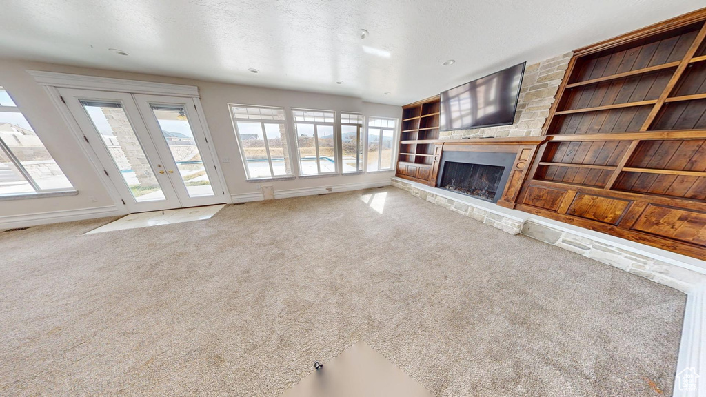 Unfurnished living room with carpet, built in shelves, french doors, and a stone fireplace