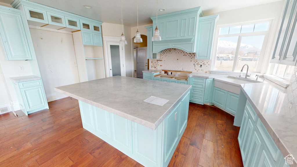 Kitchen with dark wood-type flooring, a kitchen island, a sink, decorative backsplash, and glass insert cabinets