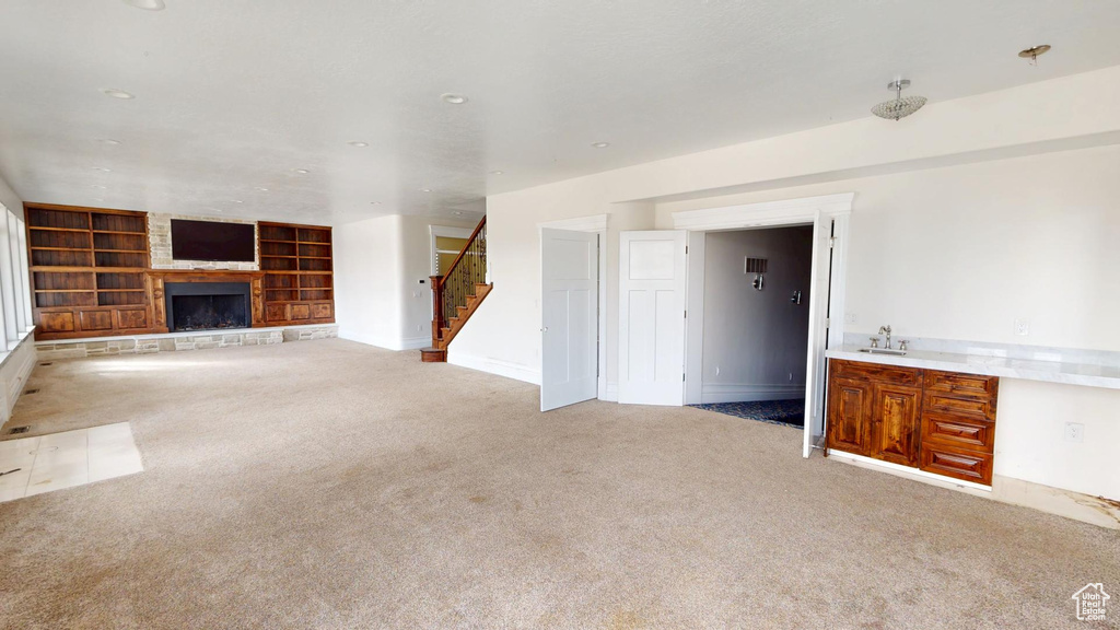 Unfurnished living room featuring built in features, light colored carpet, a large fireplace, a sink, and stairs