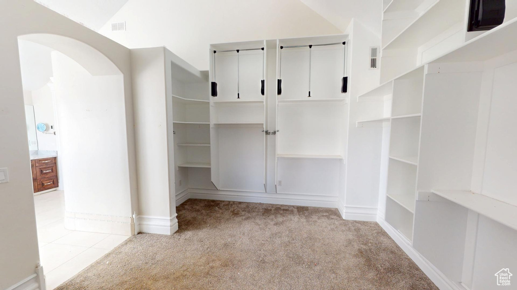 Spacious closet with arched walkways, carpet floors, vaulted ceiling, and visible vents