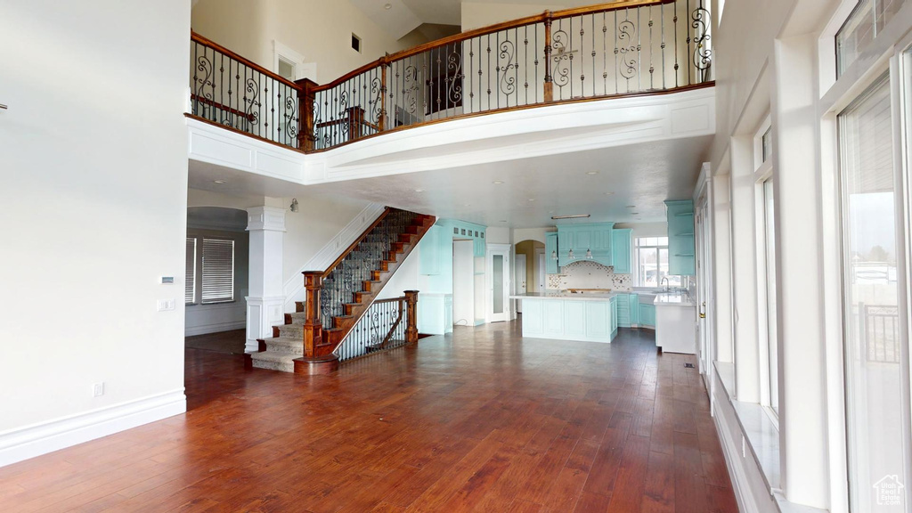 Unfurnished living room featuring a towering ceiling, ornate columns, stairs, and dark wood finished floors