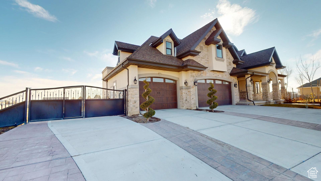 View of front of house featuring stone siding, driveway, a gate, and stucco siding