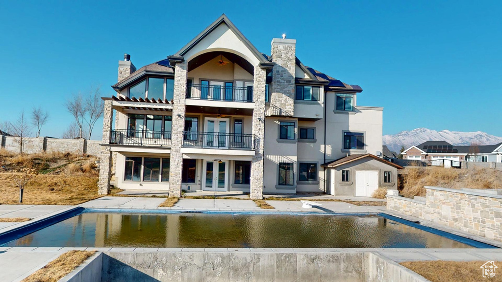 Back of property with french doors, a chimney, a balcony, and stucco siding