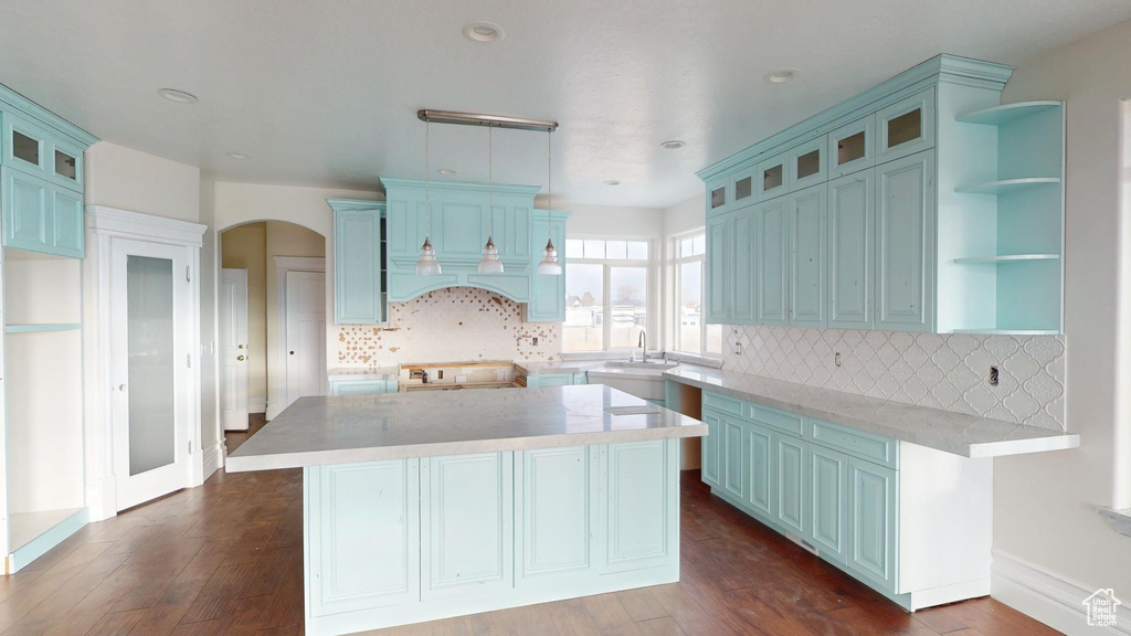 Kitchen featuring arched walkways, a center island, open shelves, dark wood-type flooring, and blue cabinets