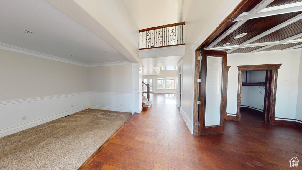 Corridor with a wainscoted wall, ornamental molding, wood finished floors, and decorative columns