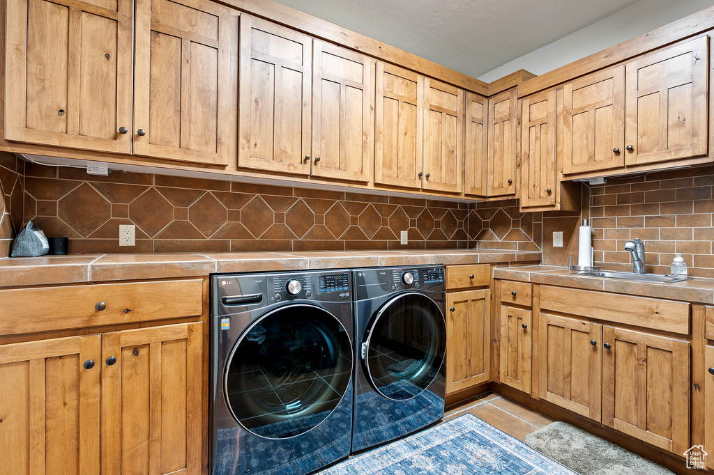 Clothes washing area with a sink, separate washer and dryer, light tile patterned floors, and cabinet space