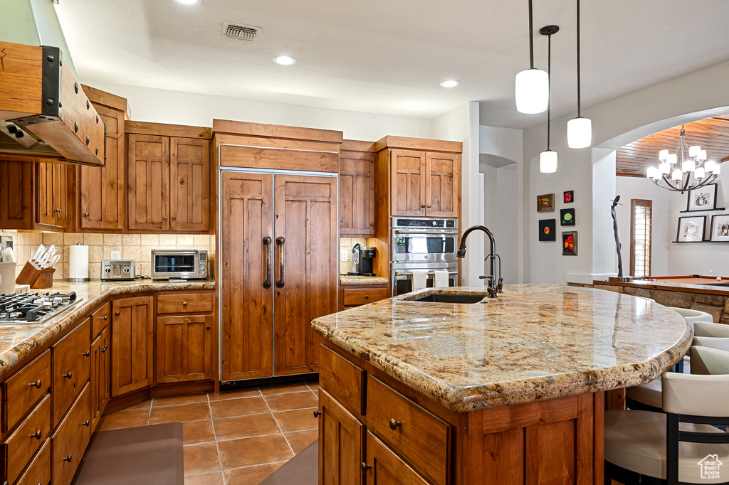 Kitchen with appliances with stainless steel finishes, a sink, arched walkways, tasteful backsplash, and visible vents