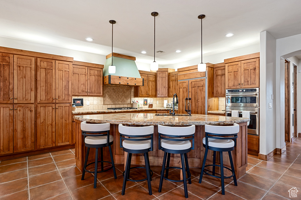 Kitchen with a center island with sink, dark tile patterned flooring, tasteful backsplash, custom range hood, and appliances with stainless steel finishes
