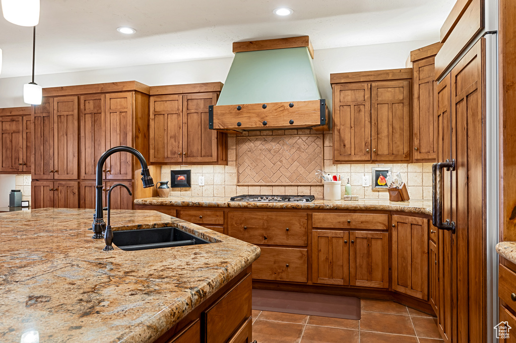Kitchen featuring a sink, range hood, brown cabinets, and tasteful backsplash