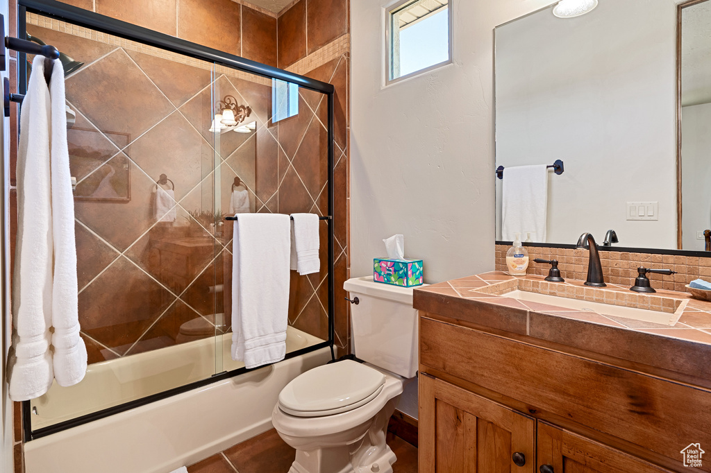 Full bath featuring vanity, bath / shower combo with glass door, and toilet