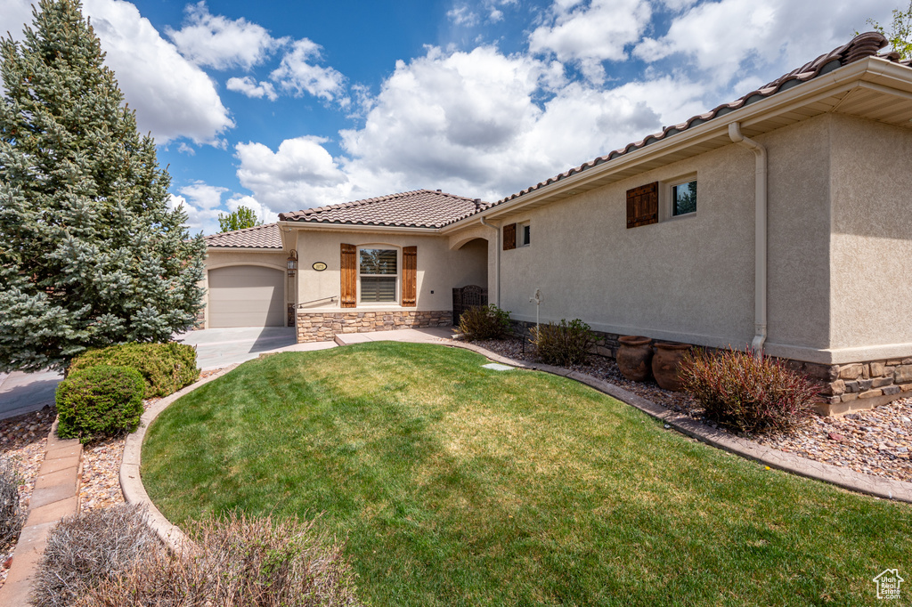 View of front of property with a tile roof, a front yard, a garage, stone siding, and stucco siding