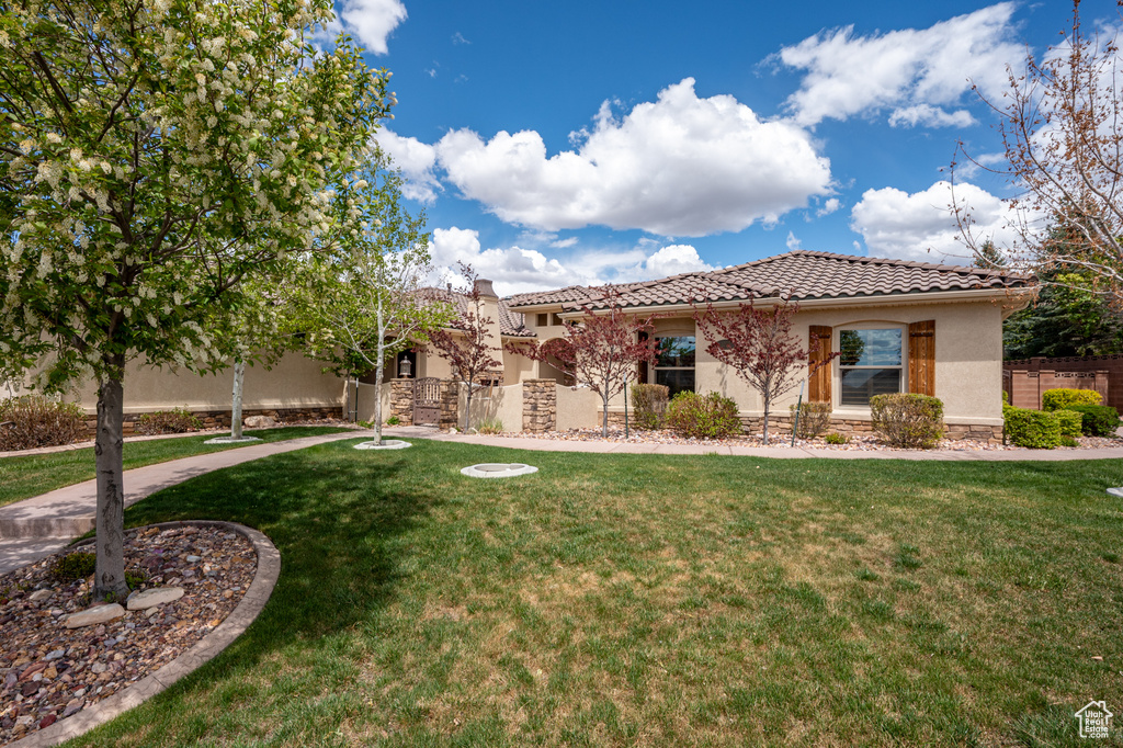 View of front of property featuring a front lawn, fence, stone siding, stucco siding, and a tiled roof