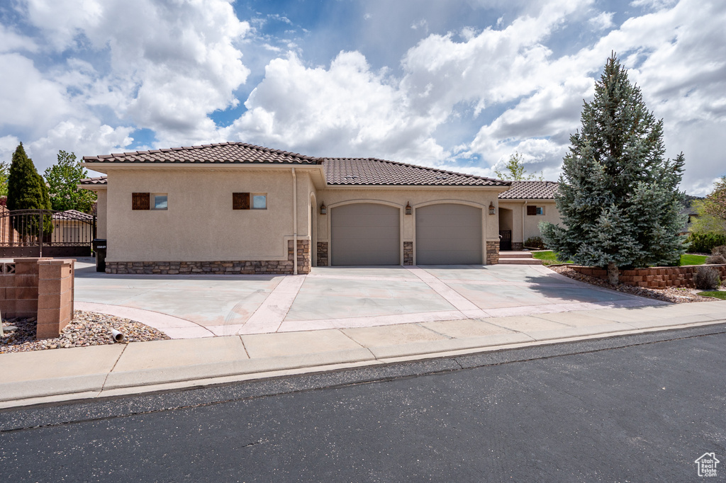 Mediterranean / spanish home with stone siding, stucco siding, a tiled roof, an attached garage, and driveway