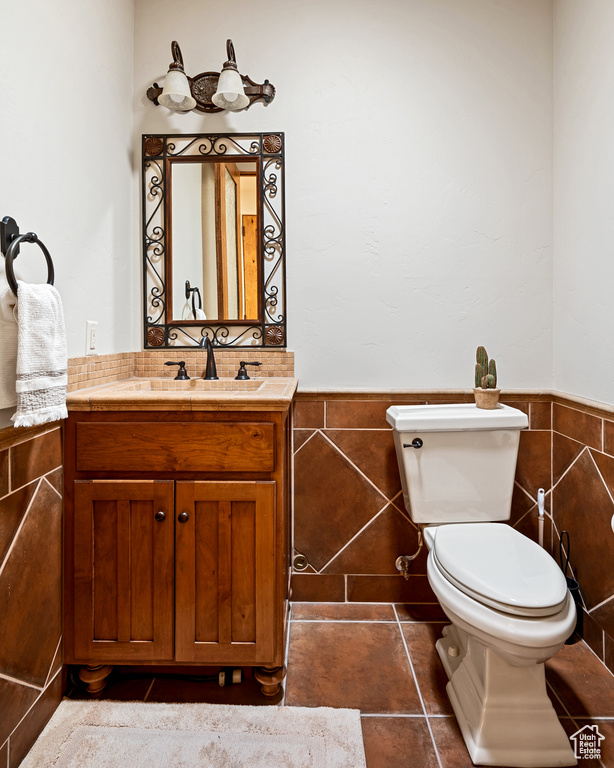 Half bath featuring vanity, wainscoting, toilet, and tile walls