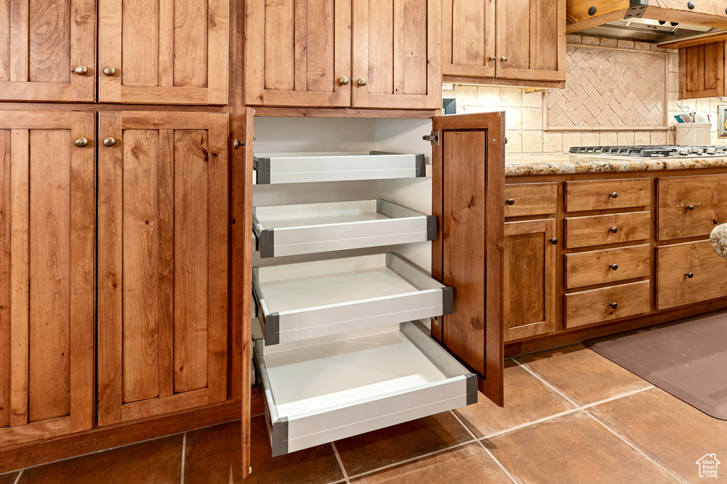 Room details featuring brown cabinets, light stone counters, stainless steel gas stovetop, tasteful backsplash, and under cabinet range hood