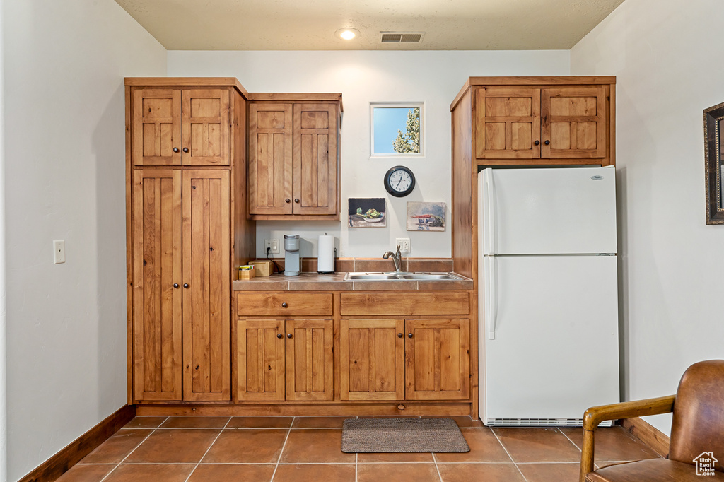 Kitchen with visible vents, brown cabinets, a sink, dark tile patterned flooring, and freestanding refrigerator