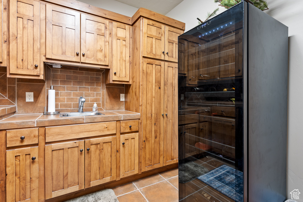 Kitchen featuring light tile patterned flooring, a sink, light countertops, black refrigerator, and decorative backsplash