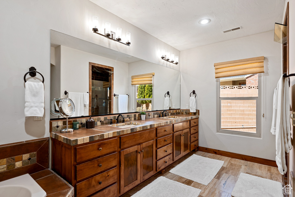 Bathroom with a sink, double vanity, wood finished floors, visible vents, and a stall shower