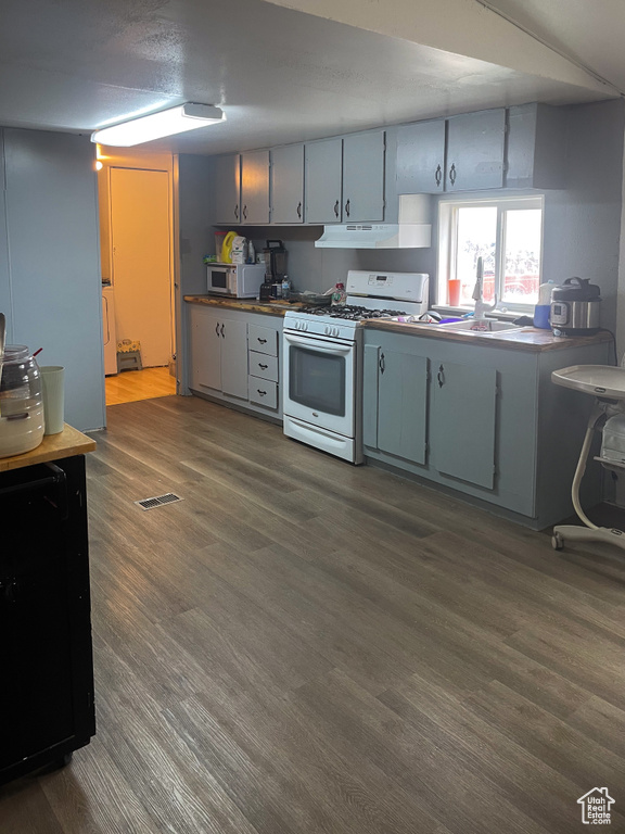 Kitchen with dark wood-style floors, stainless steel microwave, gas range gas stove, under cabinet range hood, and a sink