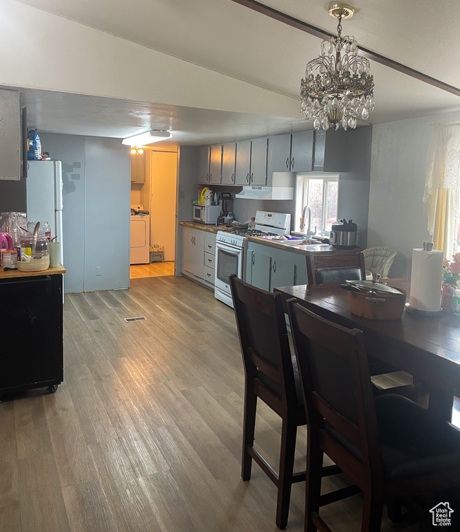 Kitchen with gas range gas stove, washer / clothes dryer, stainless steel microwave, light wood-type flooring, and under cabinet range hood