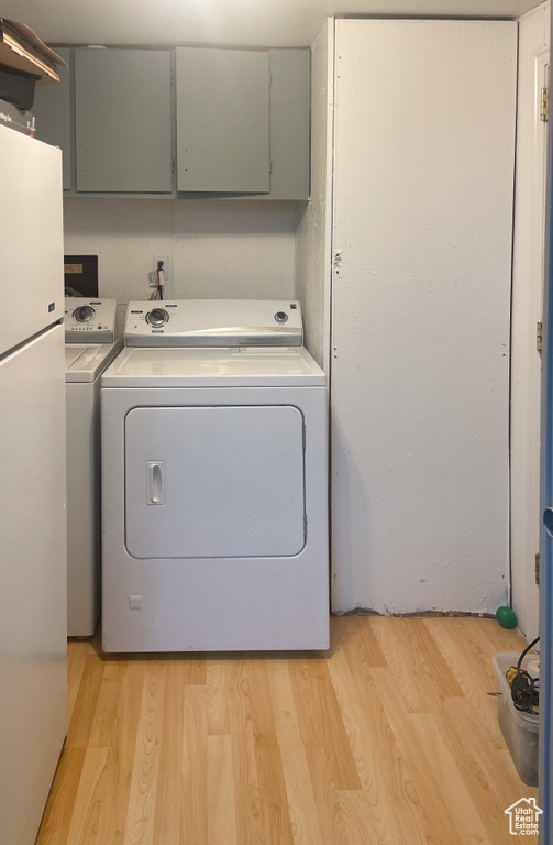 Laundry room with washer and clothes dryer, light wood-type flooring, and cabinet space