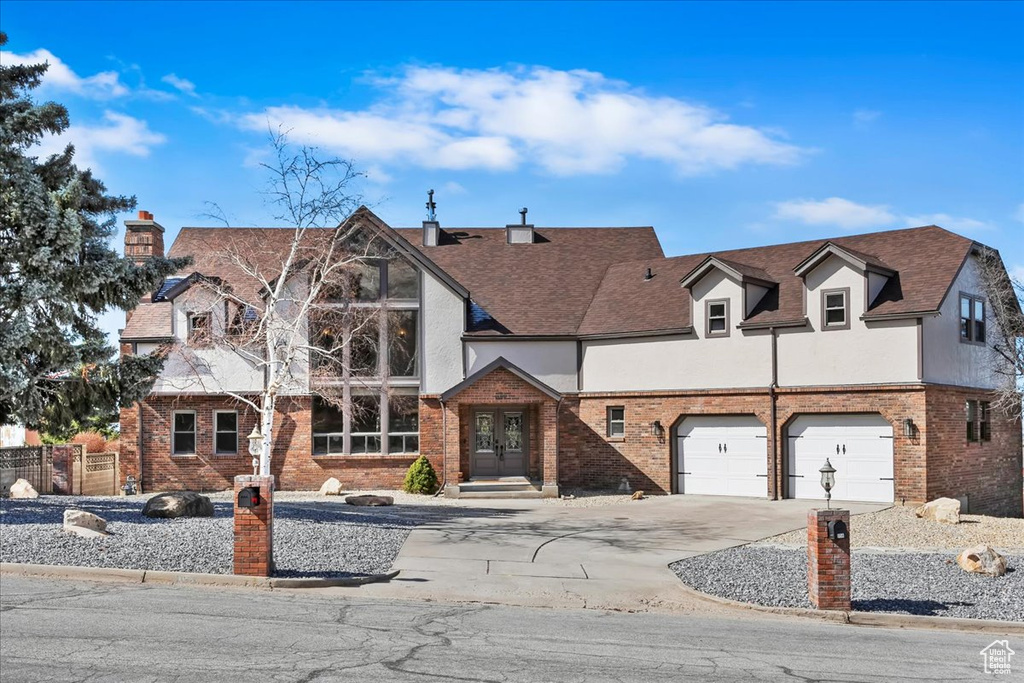 English style home with concrete driveway, french doors, brick siding, and stucco siding