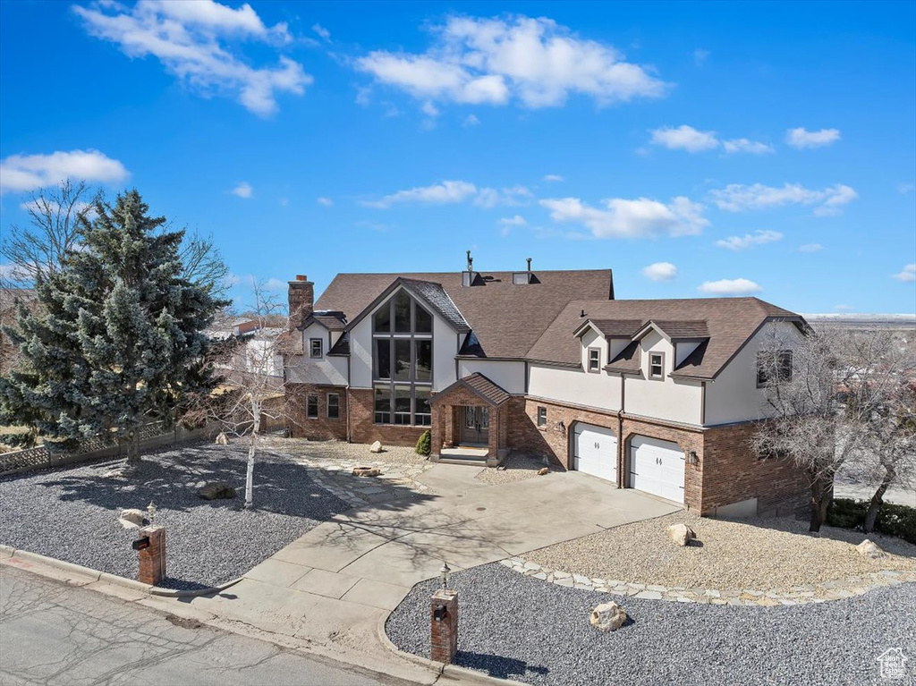 Tudor house featuring brick siding, a chimney, a shingled roof, a garage, and driveway